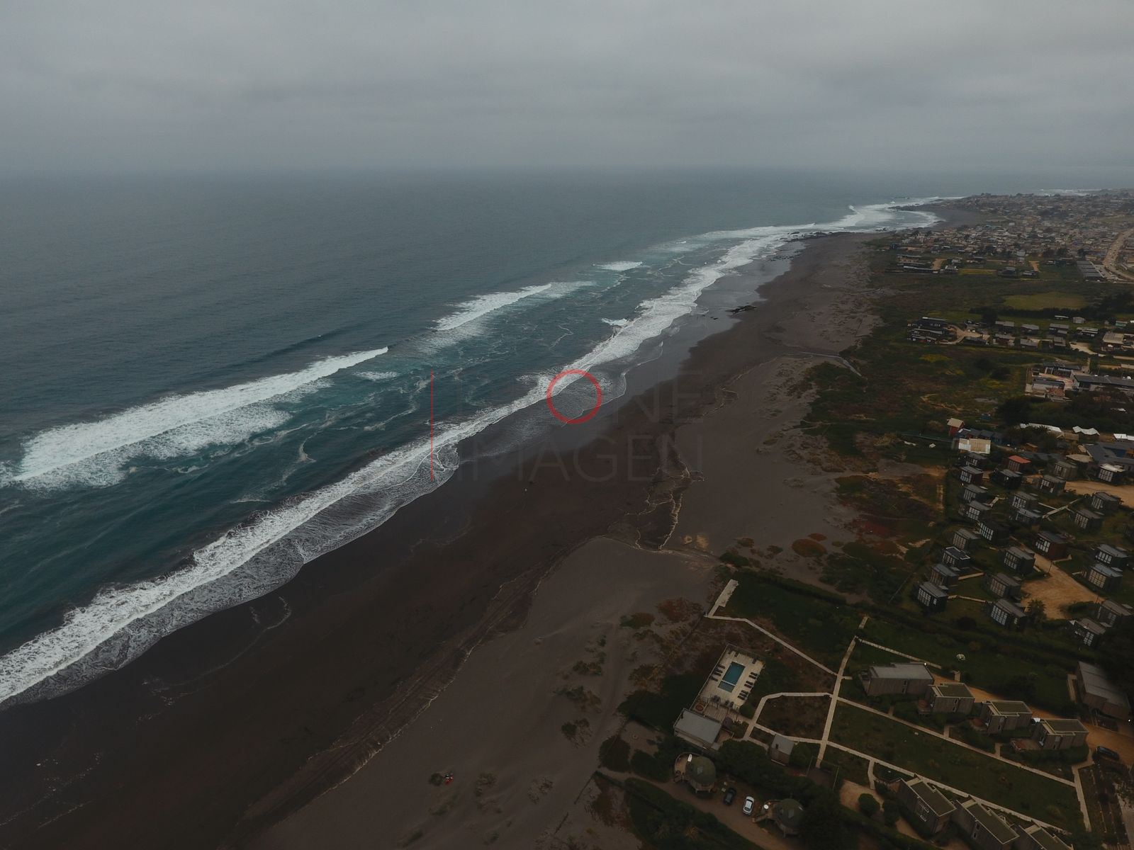 Playa de arena oscura y caserío, Pichilemu