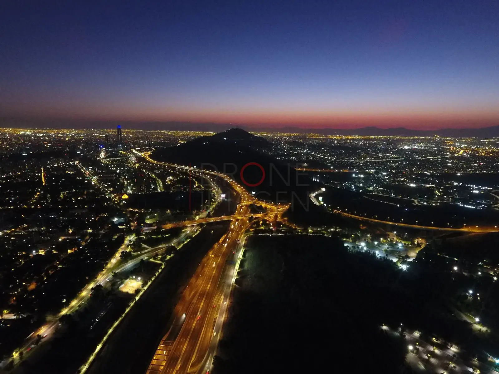 Cerro, autopista y ciudad al crepúsculo, Vitacura · vista aérea oblicua