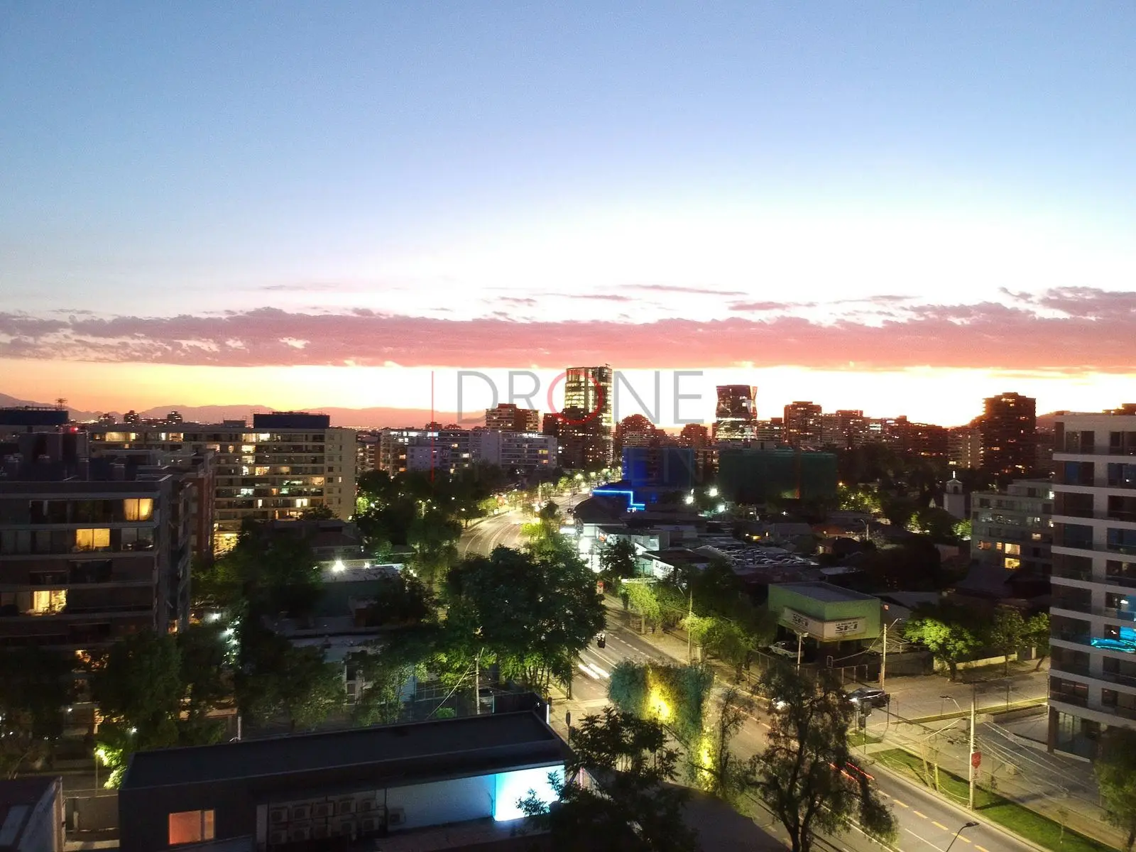 Calle iluminada bajo cielo naranja, Las Condes · vista aérea oblicua
